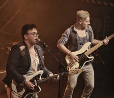 Zwei Musiker - links vorne mit E-Gitarre, rechts daneben mit E-Bass.
