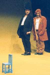 Bühnenszene der Theaterwerkstatt Hannover: im Vordergrund ein kleiner blauer Stuhl, weiter hinten ein schwarz gekleideter Mann mit Zylinder und ein braun gekleideter Mann