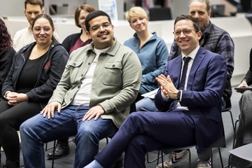 Niedersachsens Minister für Wissenschaft und Kultur Falko Mohrs sitzt zwischen Studierenden der Hochschule Emden/Leer und applaudiert lachend.