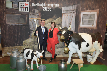 Niedersachsens Minister für Wissenschaft und Kultur Falko Mohrs gemeinsam mit Pressesprecherin Julia Streuer beim Neujahrsempfang des Radiosenders ffn. Mohrs hält eine Mistgabel neben einer Plastikkuh hoch und lächelt.