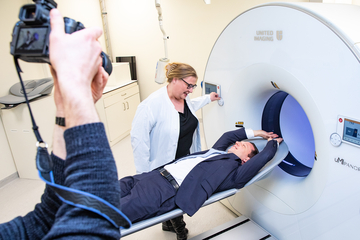 Niedersachsens Minister für Wissenschaft und Kultur Falko Mohrs liegt in der Röhre des neuen Total-Body-PET an der Medizinischen Hochschule Hannover. Er hat die Arme über den Kopf erhoben und lächelt einer Mitarbeitenden zu.