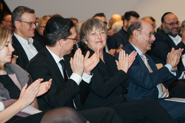 Minister Falko Mohrs applaudiert im Publikum bei der Gedenkveranstaltung des Landesverbandes der Jüdischen Gemeinden von Niedersachsen. Er schaut zu Landtagspräsidentin Hanna Naber neben ihm.