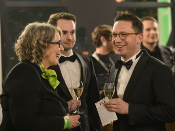 Minister Falko Mohrs steht lachend im Anzug beim Opernball in Hannover. Er hält ein Sektglas in der Hand.