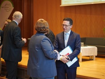 Minister Falko Mohrs unterhält sich mit einer Frau vor dem Podium bei der Auftaktveranstaltung des Verbundsprojekts agri:change
