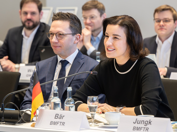 Minister Falko Mohrs sitzt neben Bundesministerin Dorothee Bär bei der Gemeinsamen Wissenschaftskonferenz in Schwerin. Mohrs lächelt zugewandt, während Bär neben ihm in ein Mikro redet.