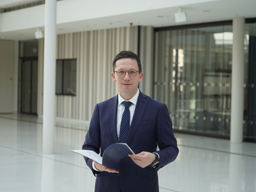 Minister Falko Mohrs steht im Niedersächsischen Landtag und blättert in einer Mappe. Er schaut lächelnd in die Kamera.