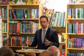 Minister Mohrs hält eine Rede beim Buchhandelspreis vor einem Regal voller bunter Kinderbücher