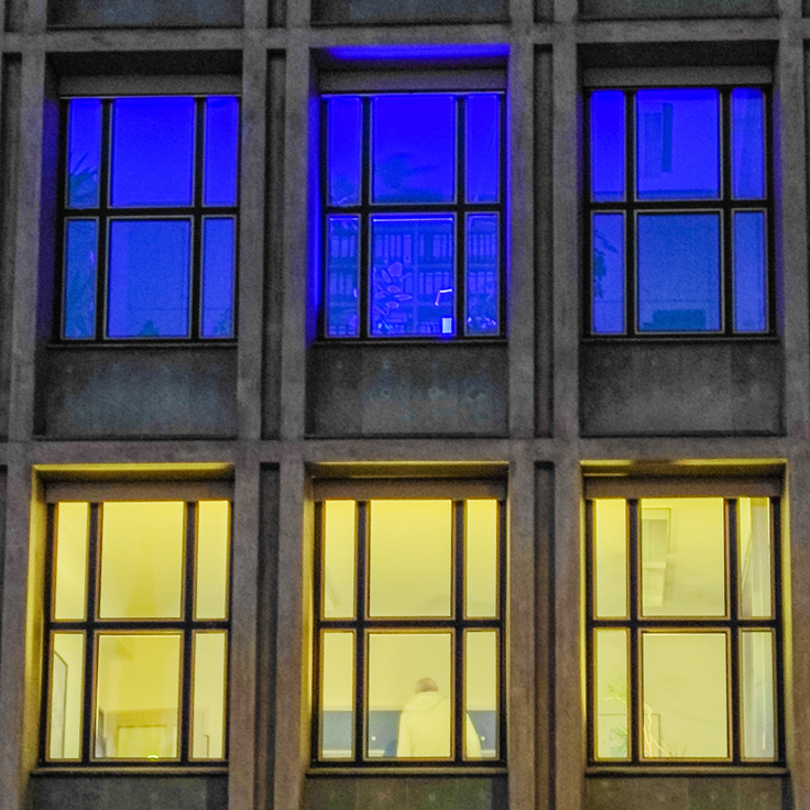 Fenster im MWK-Gebäude leuchten gelb und blau.