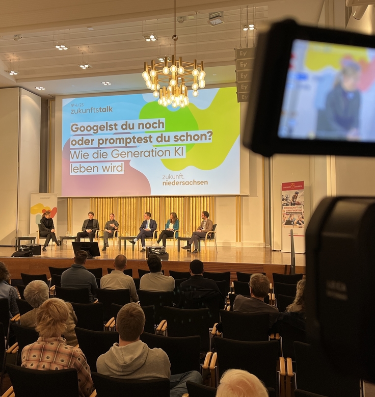 Minister Falko Mohrs und Forschende diskutieren auf der Bühne der Aula in der TU Osnabrück.