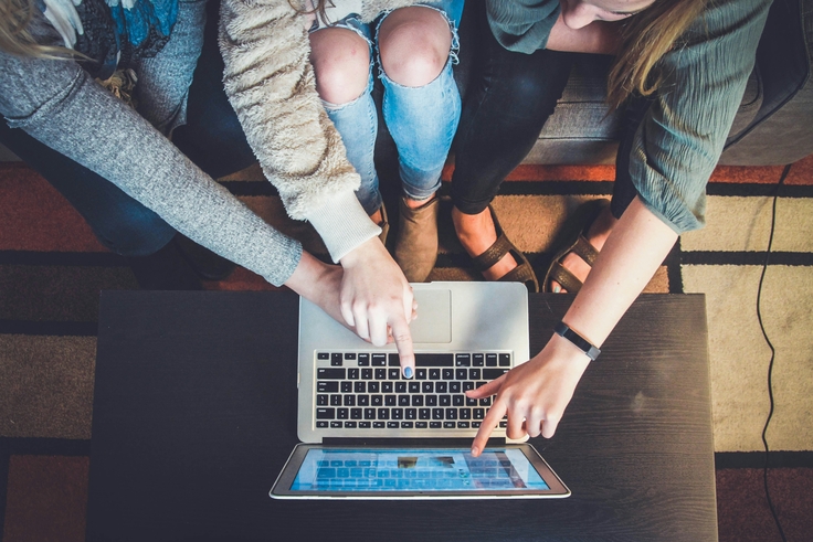 Mehrere Personen sitzen um einen Laptop und zeigen gemeinsam auf den Bildschirm, um digitale Inhalte zu besprechen.
