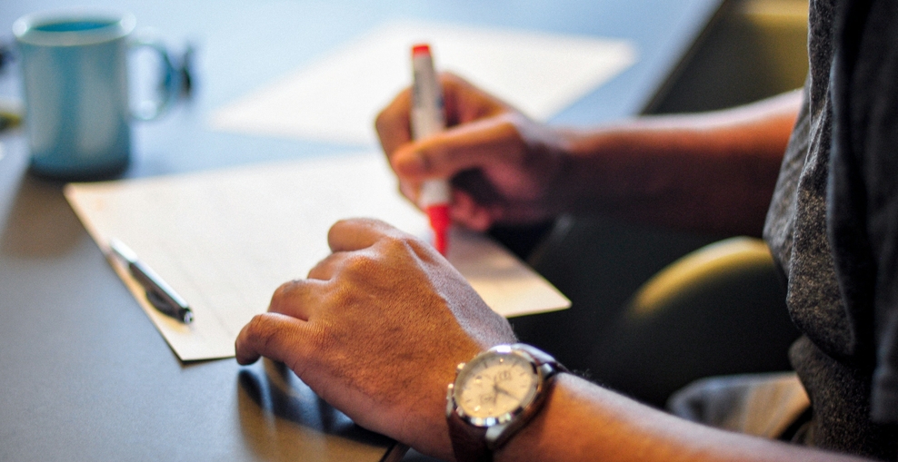 Das Bild zeigt eine Hand, die einen Stift hält und damit etwas in einem Text markiert