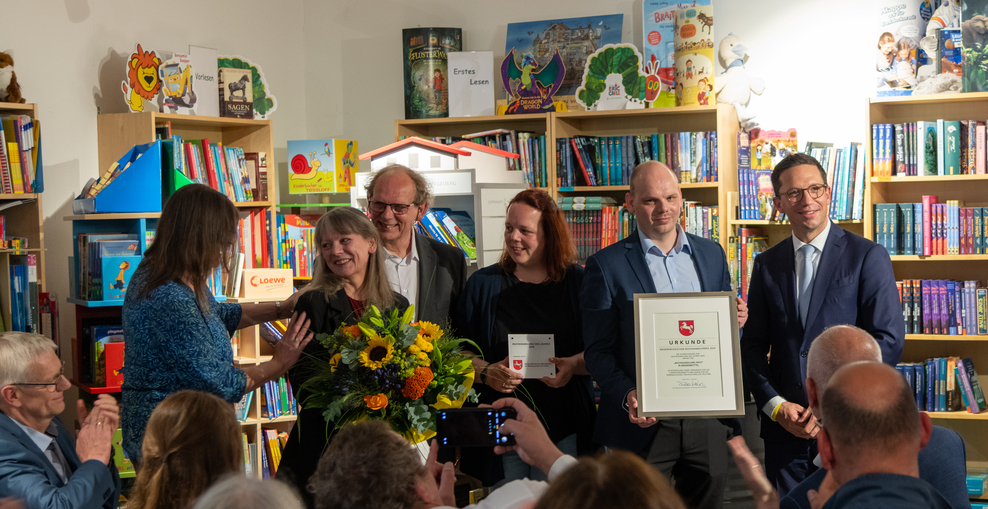 Das Team der Buchhandlung Patz steht vor dem Publikum und nimmt in seinem Buchladen den Buchhandelspreis 2026 von Minister Falko Mohrs entgegen.