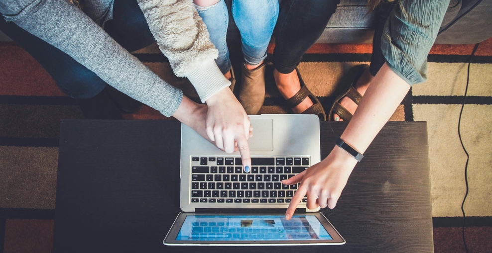 Mehrere Personen sitzen um einen Laptop und zeigen gemeinsam auf den Bildschirm, um digitale Inhalte zu besprechen.