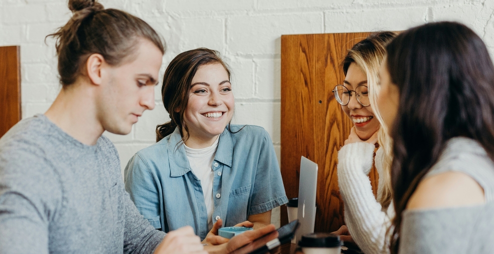 Schmuckbild: Eine Gruppe junger Menschen sitzt an einem Tisch. Die Menschen lachen und arbeiten gemeinsam an Tablet-PCs