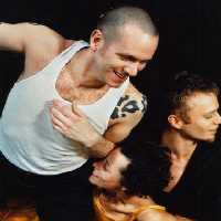 Szene des Tanztheaters International: ein Tänzererhmd im weißen Unterhemd, daneben ein Mann im schwarzen Hemd, beide in Bewegung
